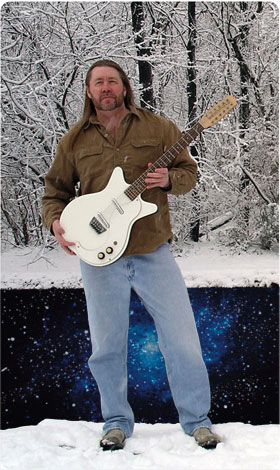 Monty Milne standing in the snow holding a white guitar.